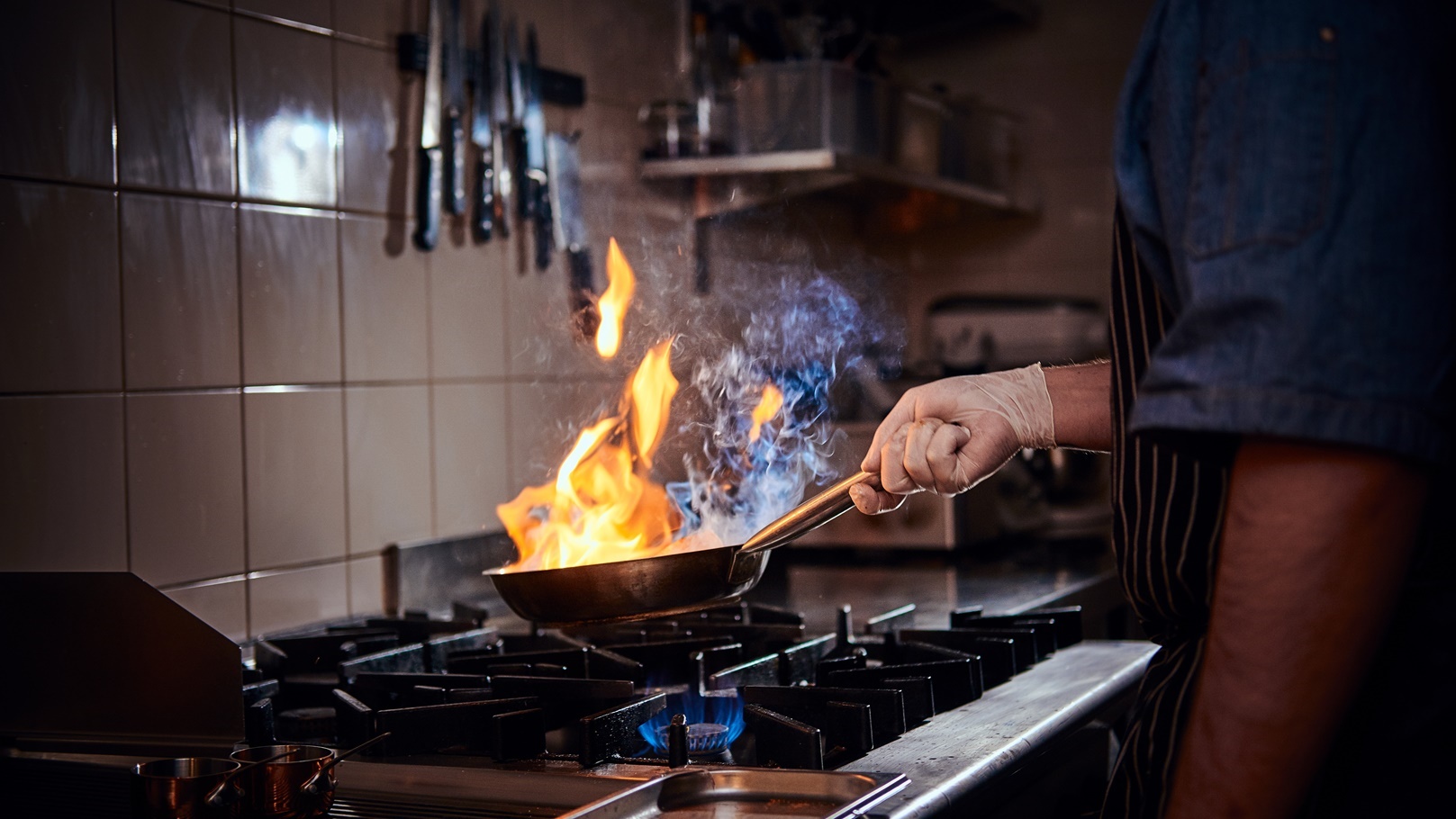 cooker-wearing-gloves-and-apron-frying-flambe-on-a-2021-08-27-23-57-19-utc