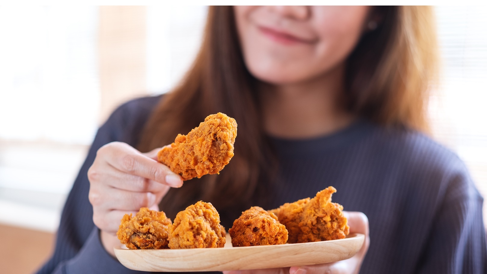 a-young-woman-holding-and-eating-fried-chicken-in-2022-01-28-10-42-07-utc