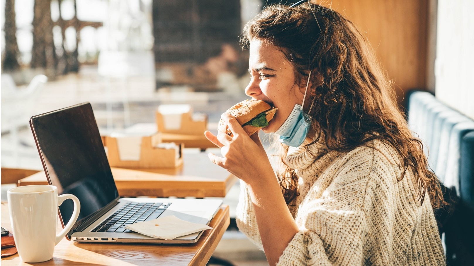woman-with-face-mask-eating-sandwich-and-using-lap-2021-08-30-00-59-14-utc