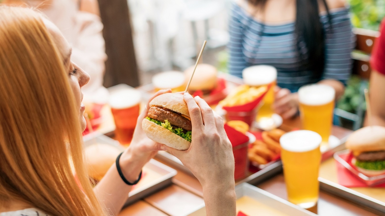 woman-with-burger-having-lunch-with-friends-2021-10-27-22-22-49-utc