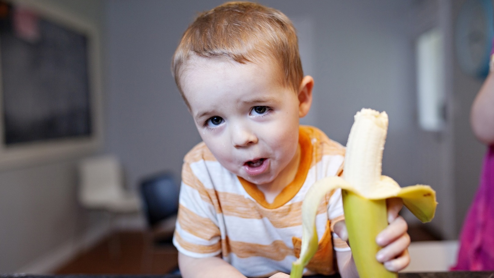 toddler-making-a-silly-face-while-eating-a-banana-2021-08-29-01-00-15-utc