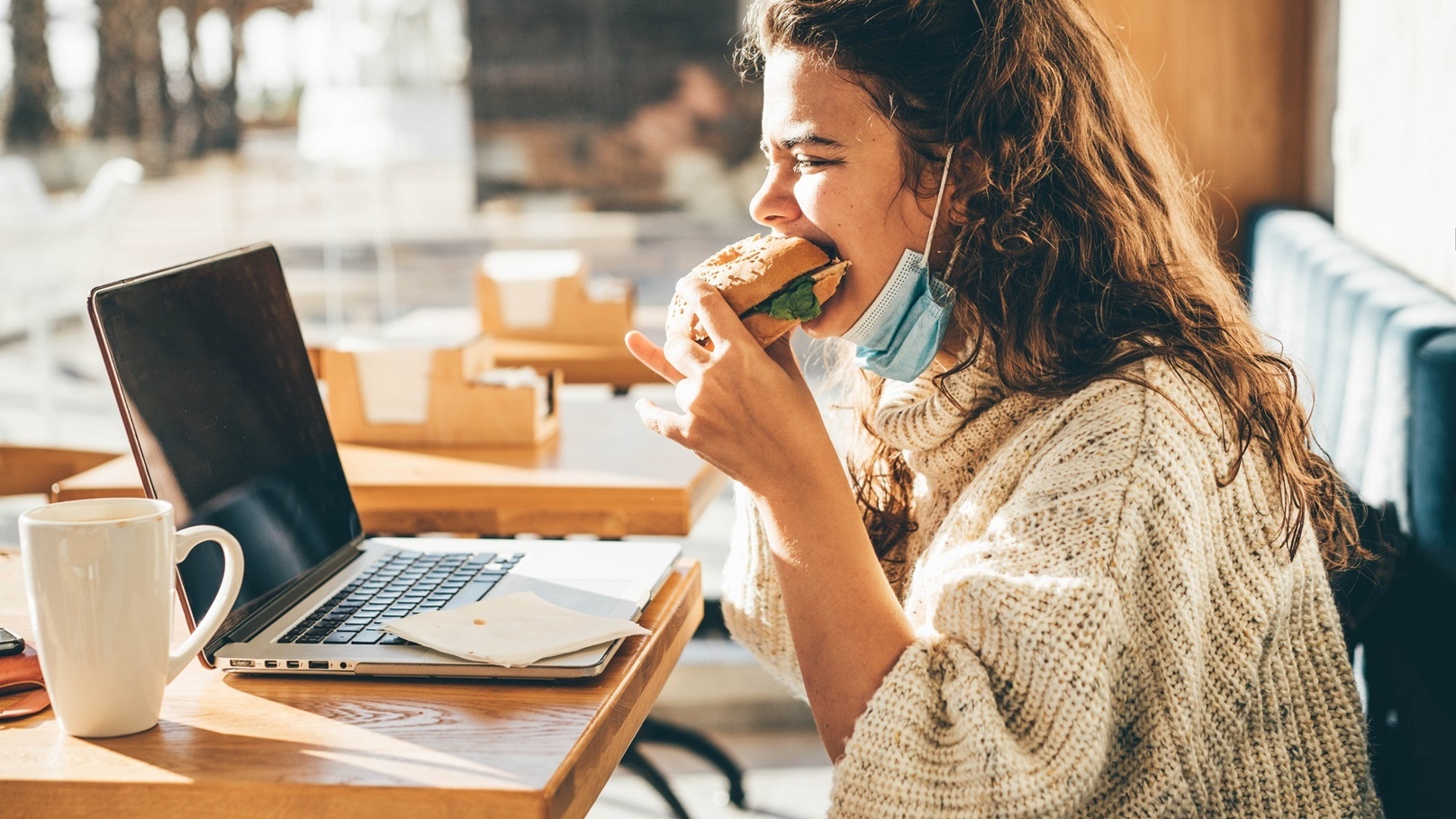 woman-with-face-mask-eating-sandwich-and-using-lap-2021-08-30-00-59-14-utc