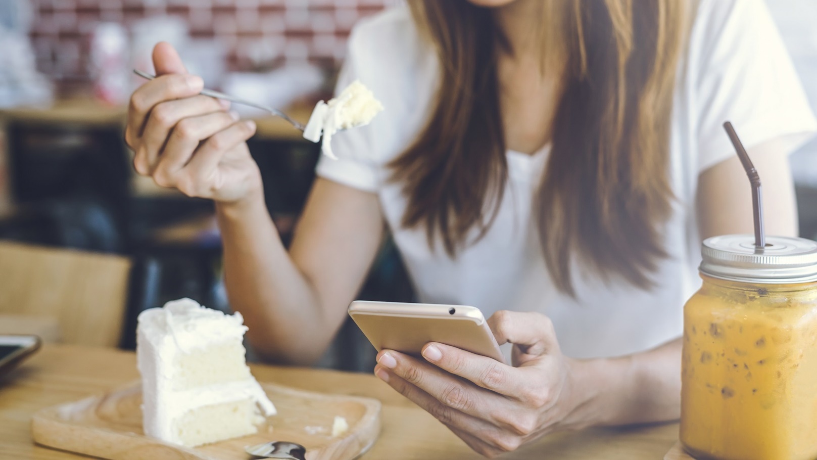 young-woman-using-smart-phone-and-eating-cake-in-c-2022-03-30-20-23-35-utc